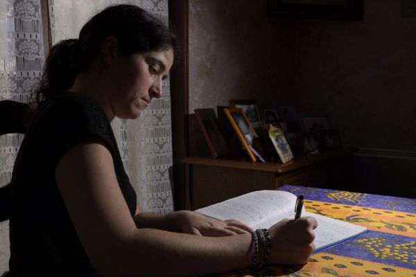 Auxiliaire de vie sociale renseignant un cahier de liaison et de soins au domicile d’un usager