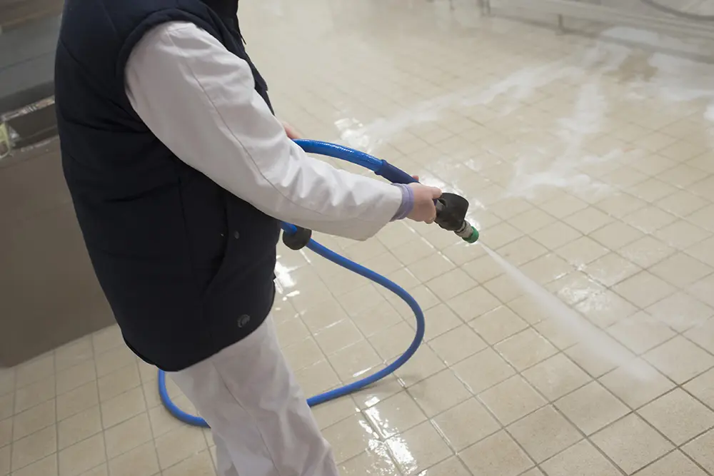 Travailleur lavant un sol en carrelage antidérapant à joint époxy dans une entreprise agroalimentaire