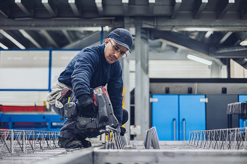 Un salarié travaille accroupi avec à la main une machine-outil 